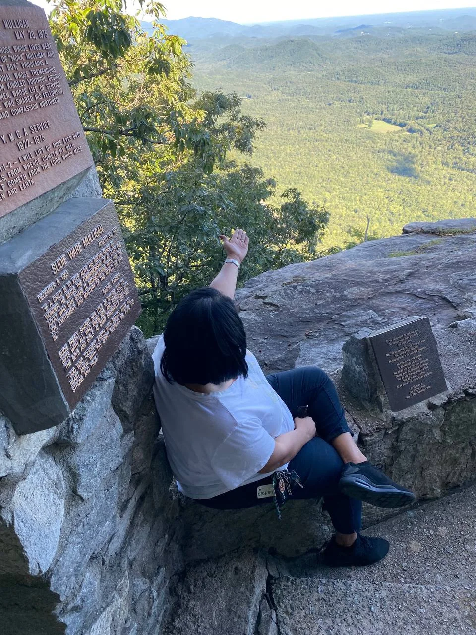 Mrs. B seated on a rocky mountain overlook, reaching toward the valley